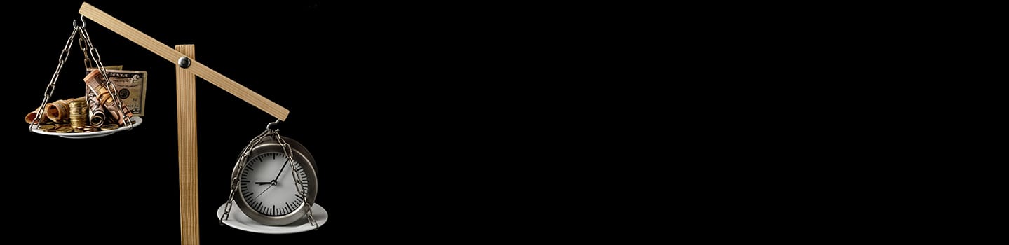 A tilted wooden balance scale weighing a pan of coins and rolled banknotes against an alarm clock on a black background